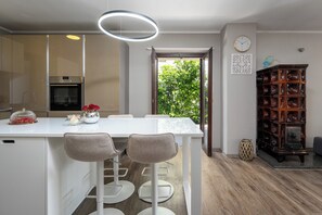 Une cuisine moderne dotée d’un four encastré, d’un îlot central blanc avec des tabourets de bar, et d’un meuble en bois contenant de la verrerie.