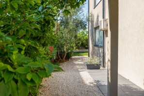 Een pad dat naar een gebouw leidt, met grind en omgeven door groen en een plant in pot.