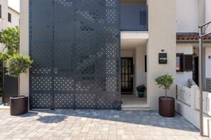 A modern building entrance with a decorative metal screen, potted plants, and a clean, paved walkway. - Family-friendly,air-conditioned, quiet location, garden, barbecue, pets welcome. (Porec)