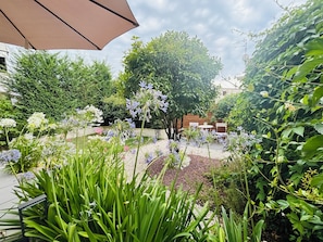 A garden with various plants and flowers, a patio area with chairs, and a large umbrella.