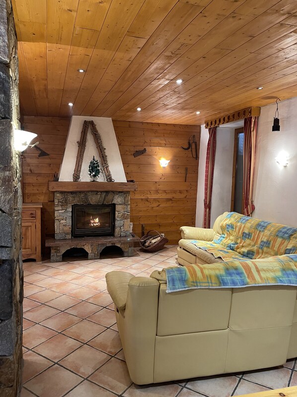 Un salon chaleureux avec une cheminée en pierre, un plafond en bois et un canapé beige.