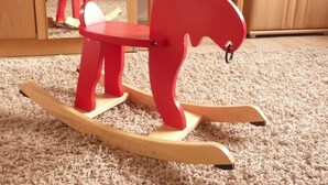 A rocking horse in a room with a carpeted floor and wooden furniture.