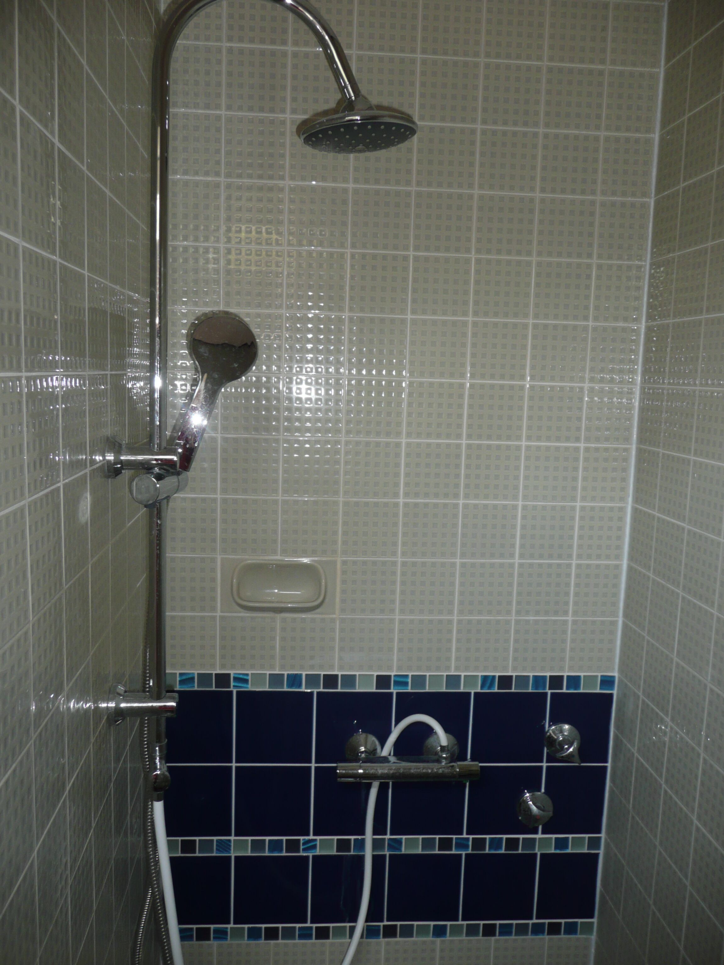 A shower with a handheld showerhead and a wall-mounted faucet.