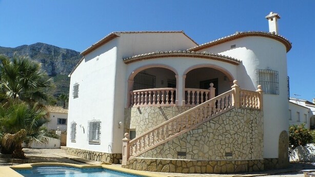 Una casa de dos pisos con piscina, fachada de piedra y un balcón con barandilla.
