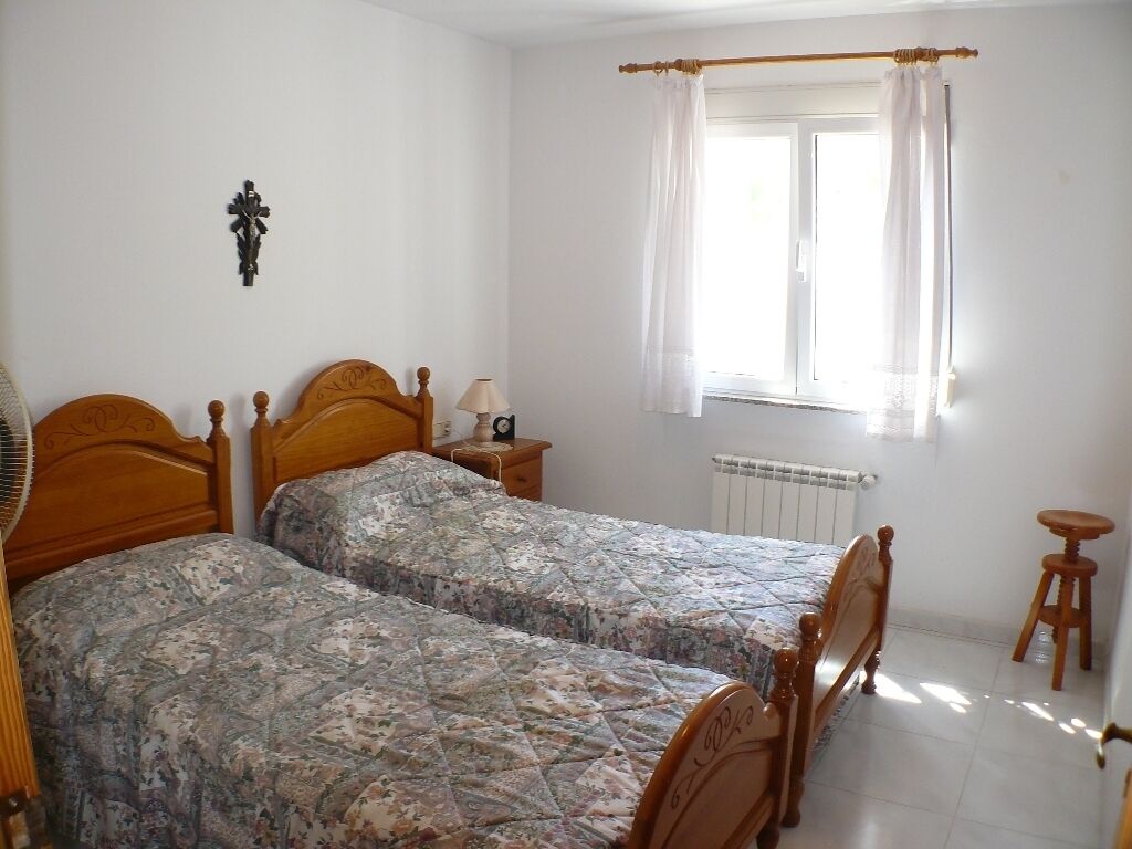 A bedroom with two wooden beds, a bedside table with a lamp, a window with curtains, and a radiator.