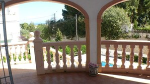 Un balcón con barandilla blanca, una planta en maceta y vistas a una piscina y follaje.