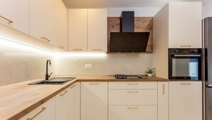 A modern kitchen with white cabinets, a wooden countertop, a built-in stove, and a stainless steel refrigerator.