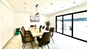 A modern dining area with a wooden table, six chairs, and a large window offering a view of the outdoors.