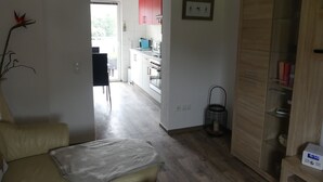 A modern kitchen with white cabinets, a red upper cabinet, and a wooden wardrobe.