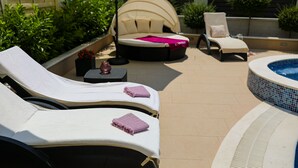 Un espace aménagé au bord de la piscine, avec des chaises longues, un jacuzzi et une petite table surmontée d’un vase.
