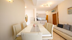 Un espace de repas moderne avec une longue table et des chaises, un canapé et une cuisine en arrière-plan.