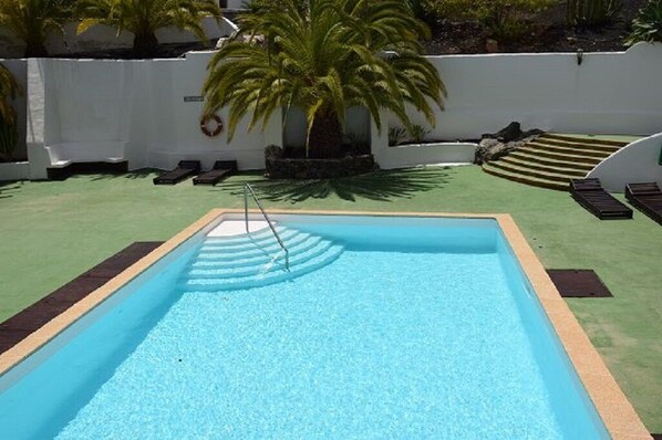 Une piscine rectangulaire à l’eau d’un bleu limpide, entourée d’une zone de gazon synthétique verdoyant.
