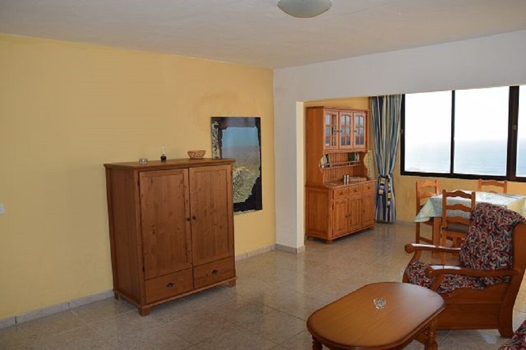 A room with a wooden cabinet, a dining table with chairs, and a view through a window.