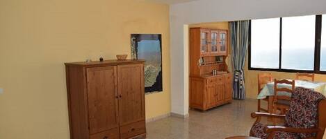 A room with a wooden cabinet, a dining table with chairs, and a view through a window.
