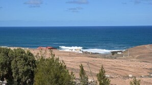 Un paisaje costero con vista despejada al mar, una playa de arena y vegetación escasa.