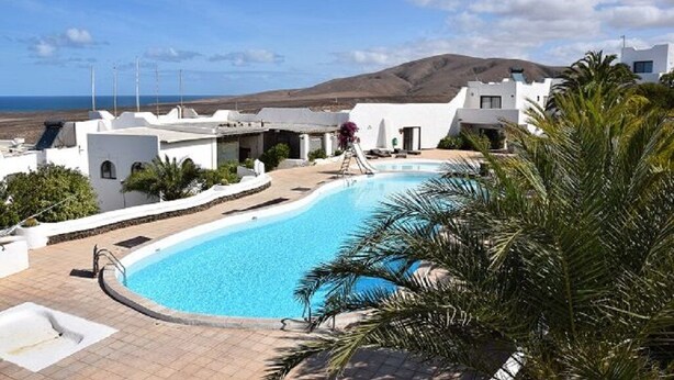 Una piscina rodeada de edificios blancos, con vista al mar y colinas al fondo.