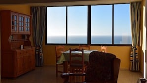 Una habitación con un amplio ventanal que ofrece vista al océano, un aparador de madera y una mesa de comedor con sillas.