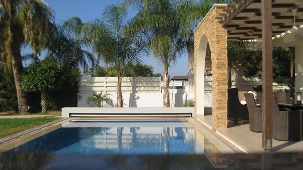 Een zwembad met een pergola en een terras.