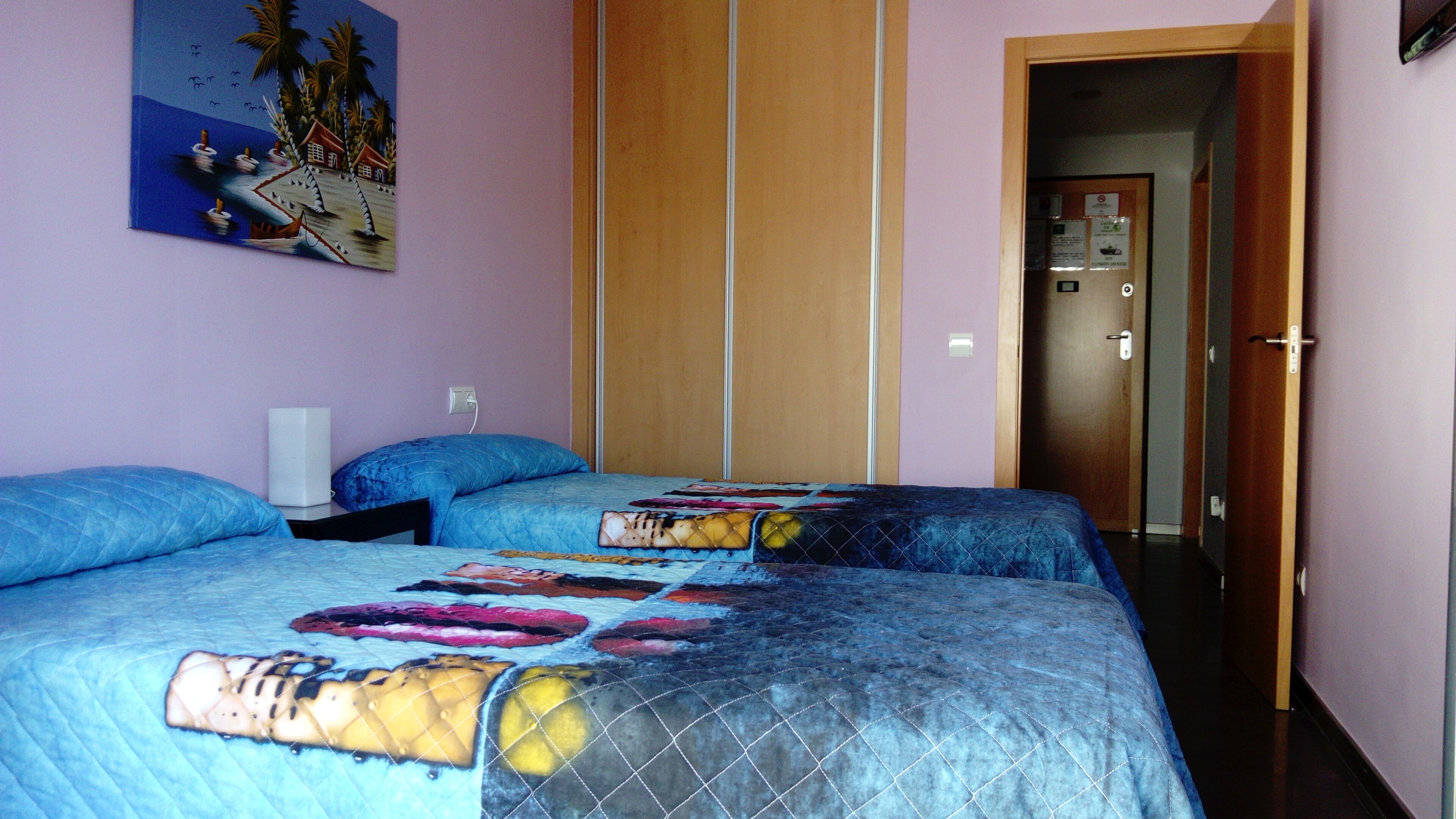 A bedroom with two beds, a nightstand, a wall-mounted lamp, and a door leading to another room.