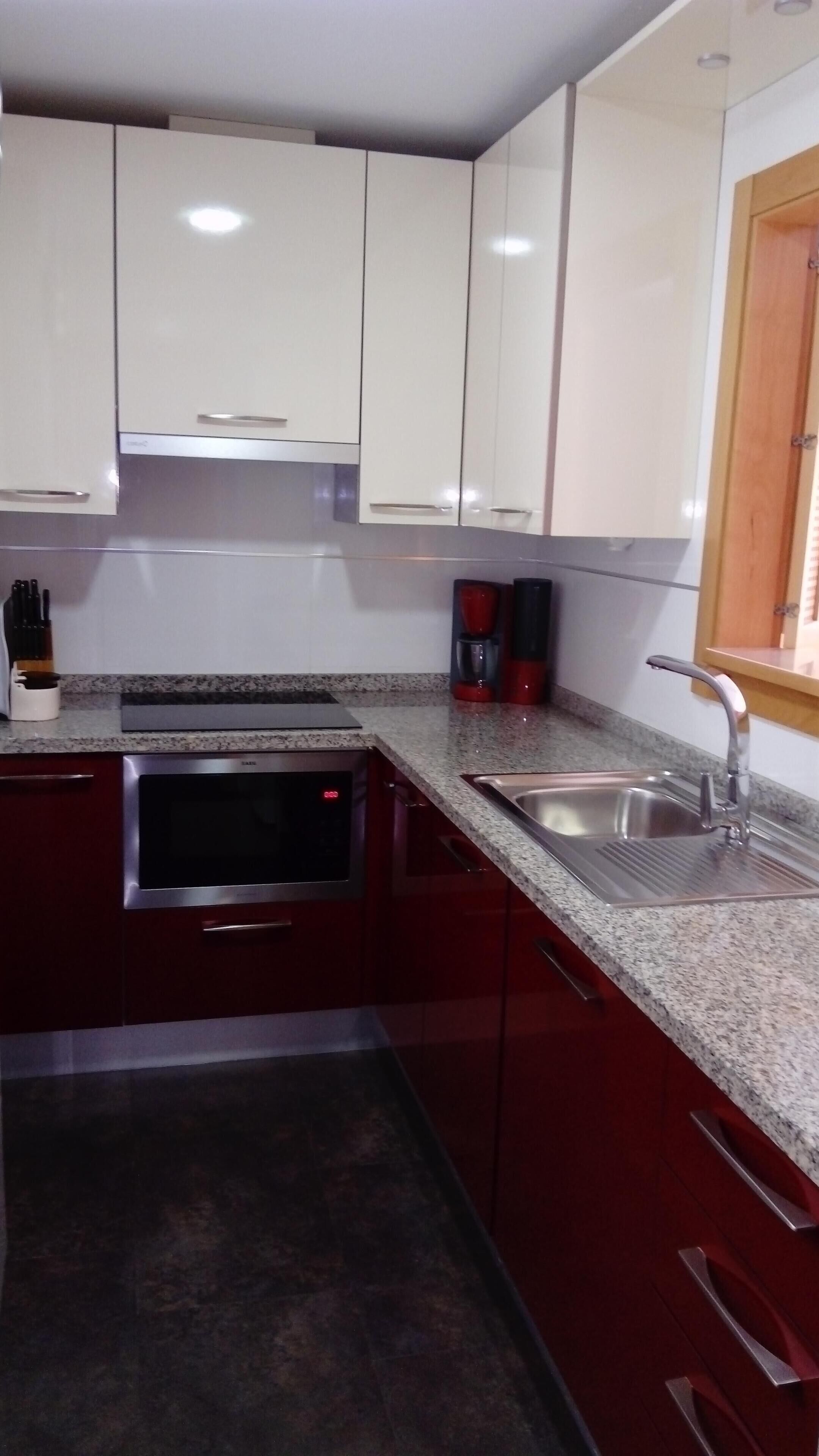 Una cocina con armarios blancos, encimera de granito, horno empotrado y un lavabo con grifo.
