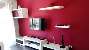 A modern living room with a flat-screen TV mounted on the wall, white shelving units, and a red accent wall. - OFFERS FOR LAST DAYS!!, LUXURY ATTIC CARIHUELA,  2 GARAGES, POOL, INT. CHANNELS (Torremolinos)