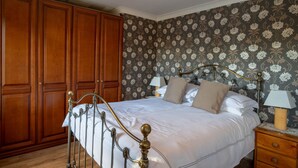 Une chambre à coucher avec une grande armoire en bois, un lit à baldaquin classique et un papier peint à motifs floraux.