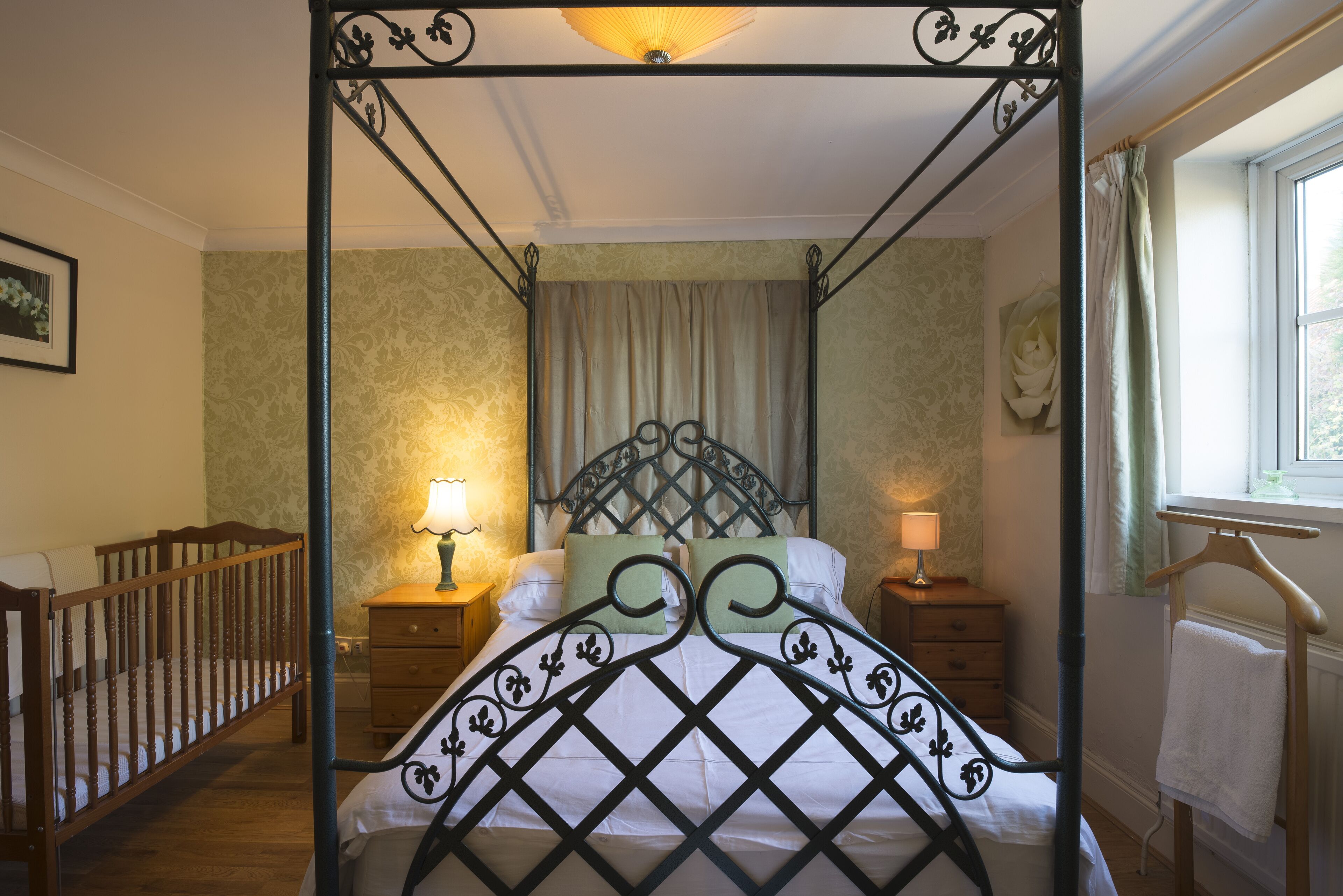 Un lit à baldaquin avec un cadre en bois, deux tables de chevet avec des lampes, un berceau en bois et une fenêtre avec des rideaux.