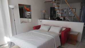 Un dormitorio con una cama, un sofá rojo, una mesita, una lámpara y una escalera.