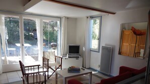 Una sala de estar con televisor, una mesita, y un sofá. Hay dos sillones y una ventana con cortinas.