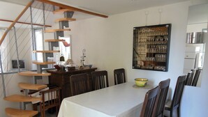 Un comedor con una mesa blanca, sillas de madera, una escalera de caracol y una estantería de pared para vinos.