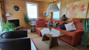 A cozy living room with wooden walls, a red sofa, a black armchair, a coffee table, and a TV.