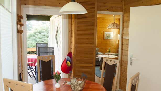 A wooden interior with a round table, chairs, a vase with flowers, and a basket.