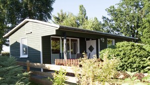 A small, single-story building with a porch and a door, surrounded by greenery.