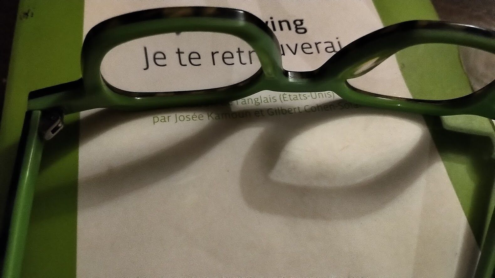 A pair of green eyeglasses resting on a piece of paper with text.