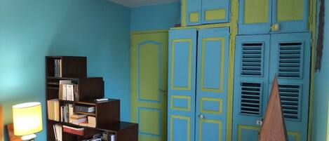 Une pièce avec une bibliothèque, une lampe et une porte ornée de panneaux bleus et jaunes.