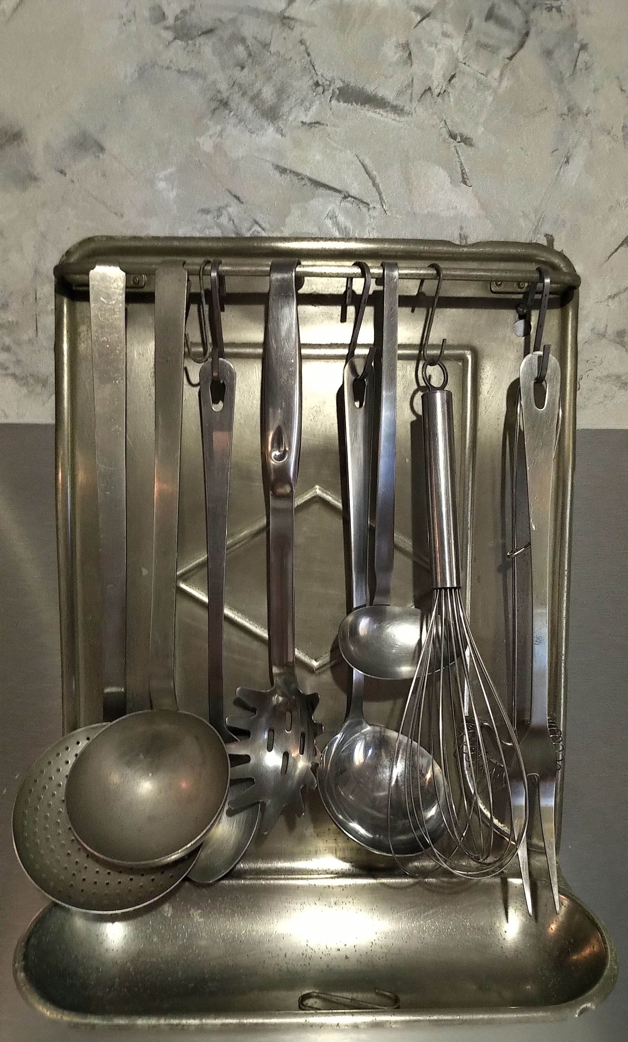 A stainless steel kitchen utensil holder with various utensils like a ladle, spatula, whisk, and tongs.