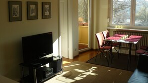 A living room with a flat-screen TV, a dining table with chairs, and a window with a view of trees.