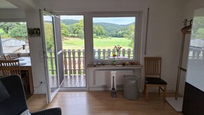 Een kamer met houten vloer, een bank, een stoel, een radiator en een raam met uitzicht op een groen landschap.