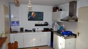 A compact kitchen with white cabinets, a stainless steel range hood, and a blue trash bin.