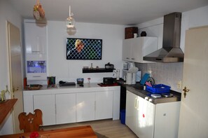 Uma cozinha compacta com armários brancos, uma coifa de aço inoxidável e uma lixeira azul.