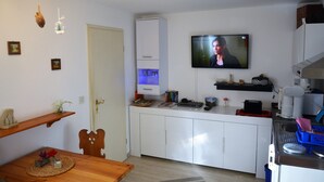 A compact kitchen with a TV mounted above the counter, a wooden dining table, and a small cabinet.