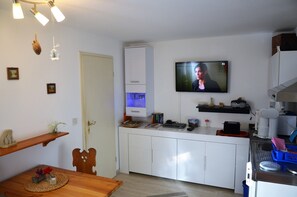 Uma cozinha compacta com uma televisão fixada acima do balcão, uma mesa de jantar de madeira e um armário pequeno.