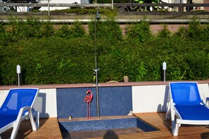 Uma área à beira da piscina com duas espreguiçadeiras azuis, uma estátua de flamingo vermelho e um poste de metal.