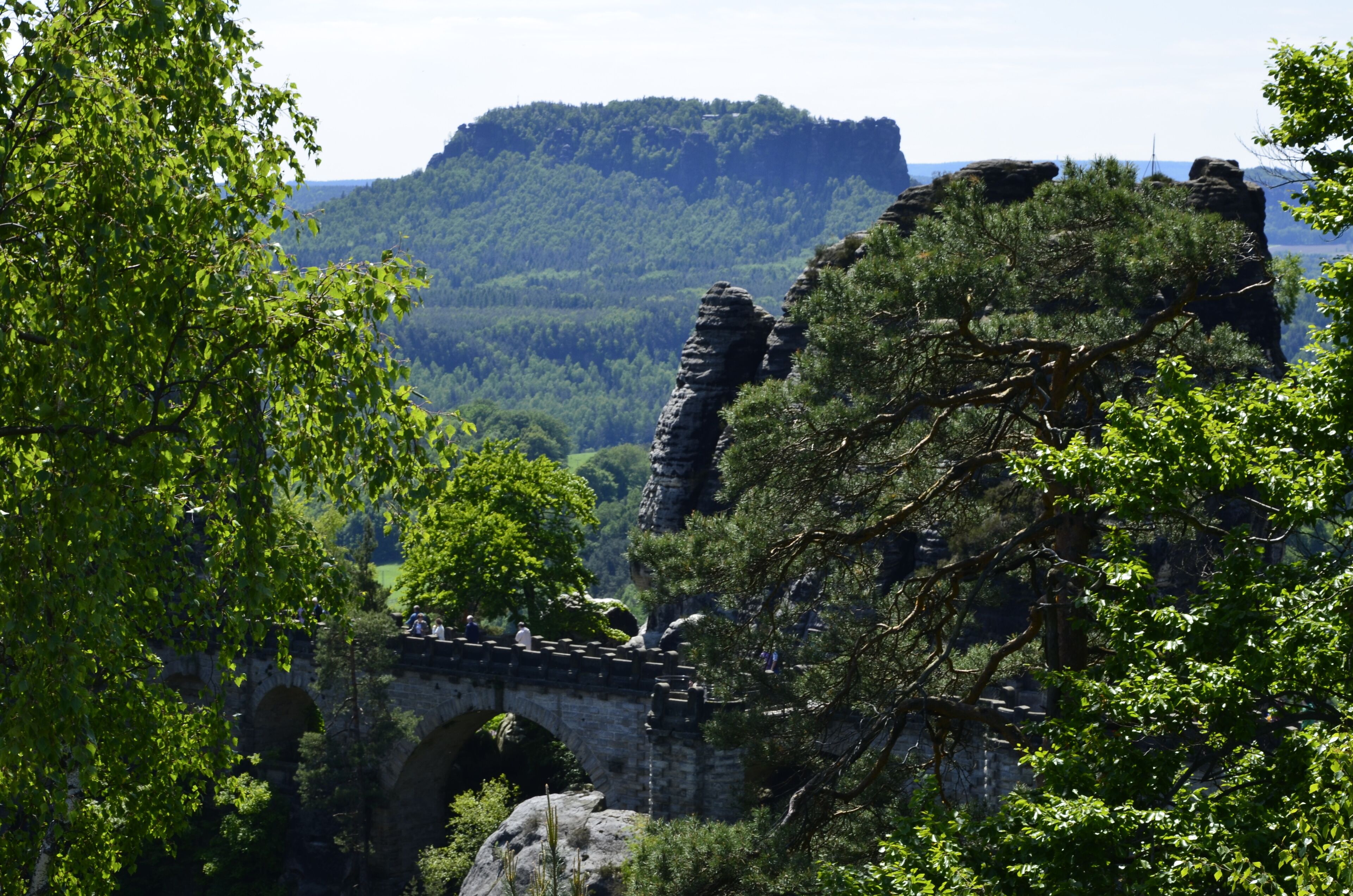 Eine Steinkonstruktion mit Bögen, umgeben von dichtem Grün und einer Berglandschaft im Hintergrund.