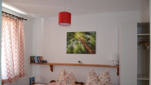 A bedroom with a bed, a shelf with books, a painting, and a red lamp.