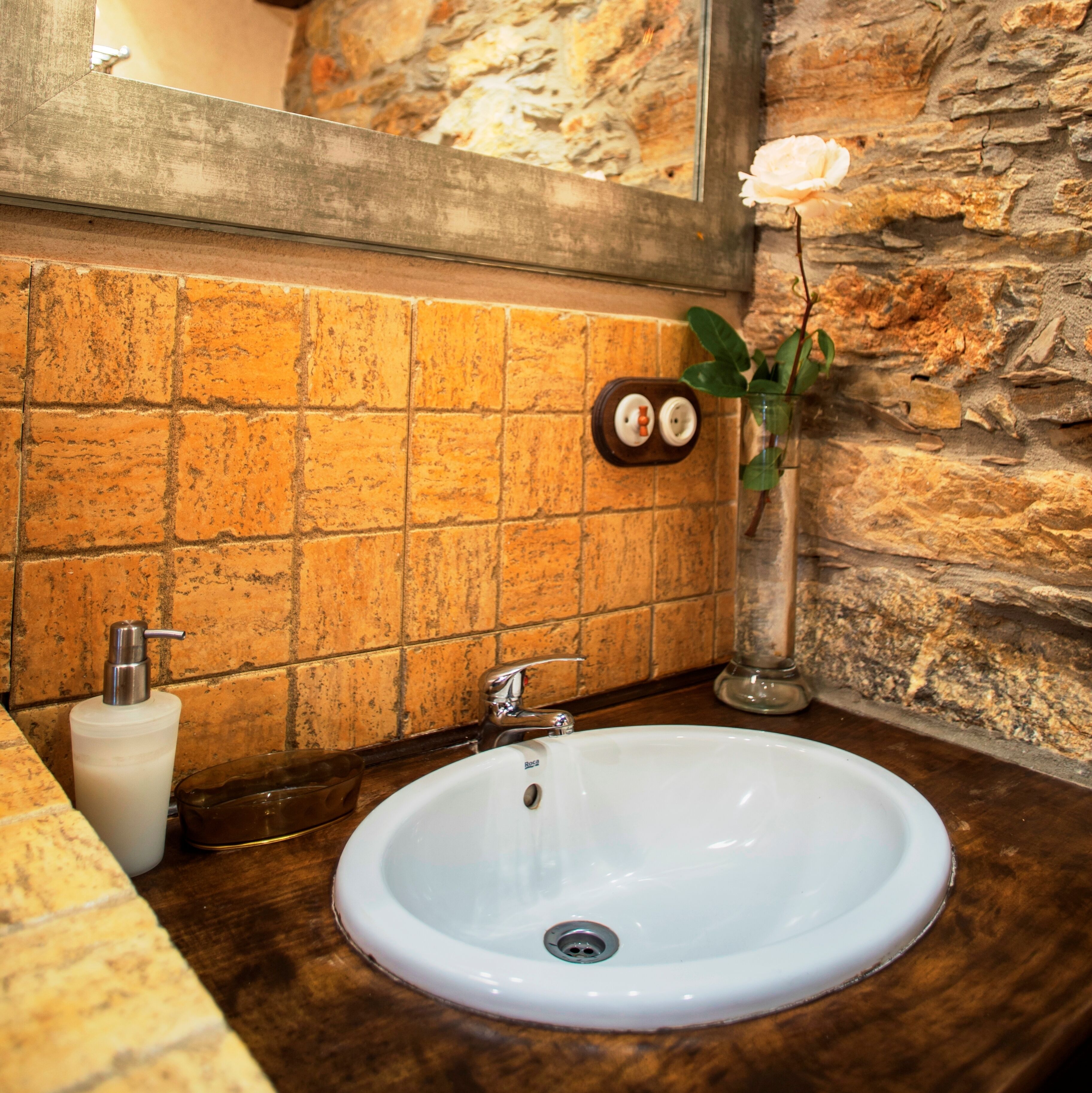 A bathroom with a white sink, a mirror, and a stone wall.