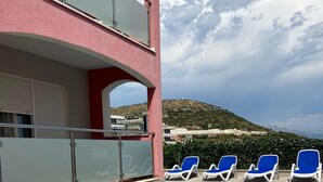 A swimming pool with blue tiles, surrounded by lounge chairs and a building with a pink facade.