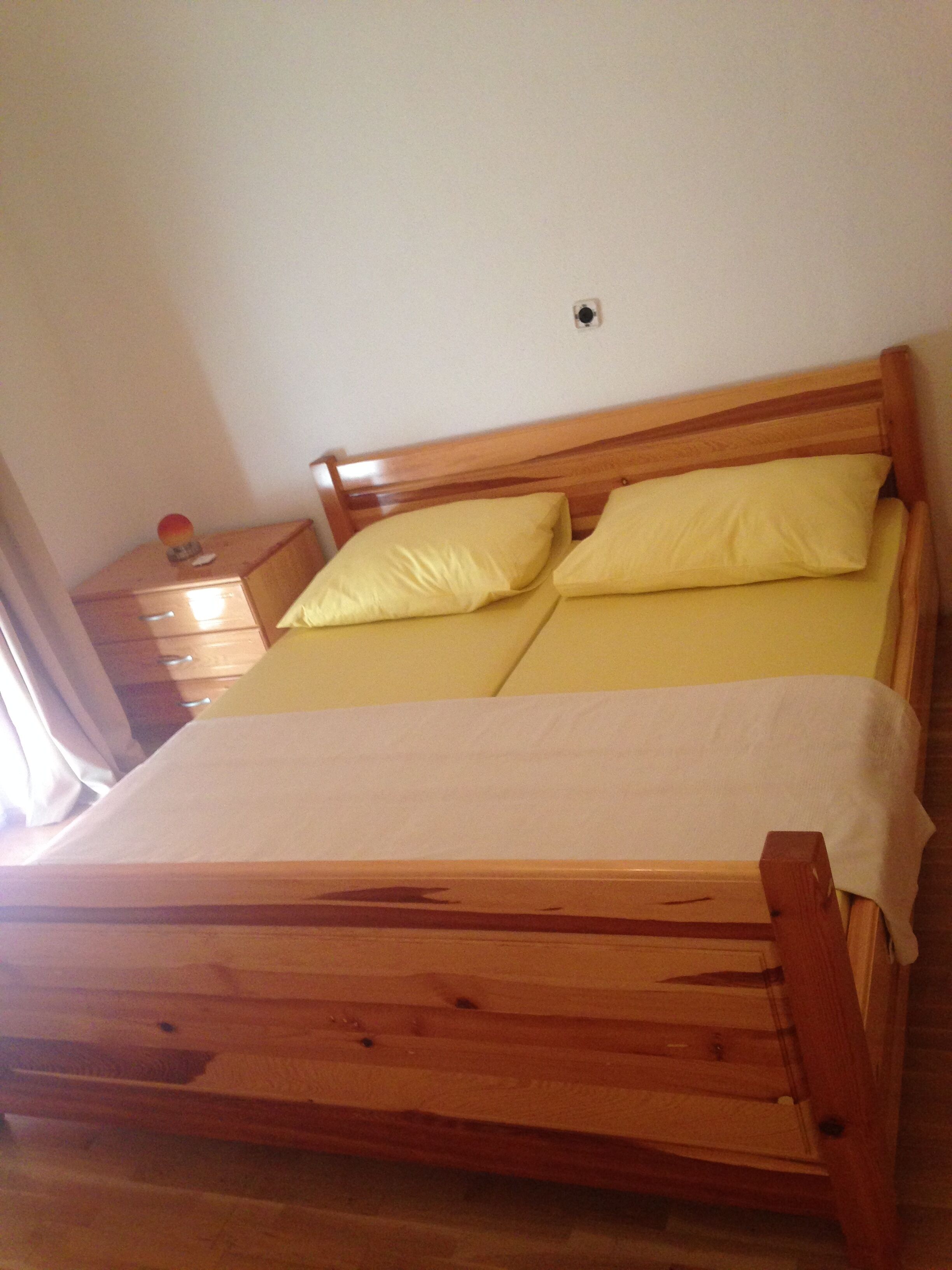 Un lit en bois avec deux oreillers et une couverture blanche.