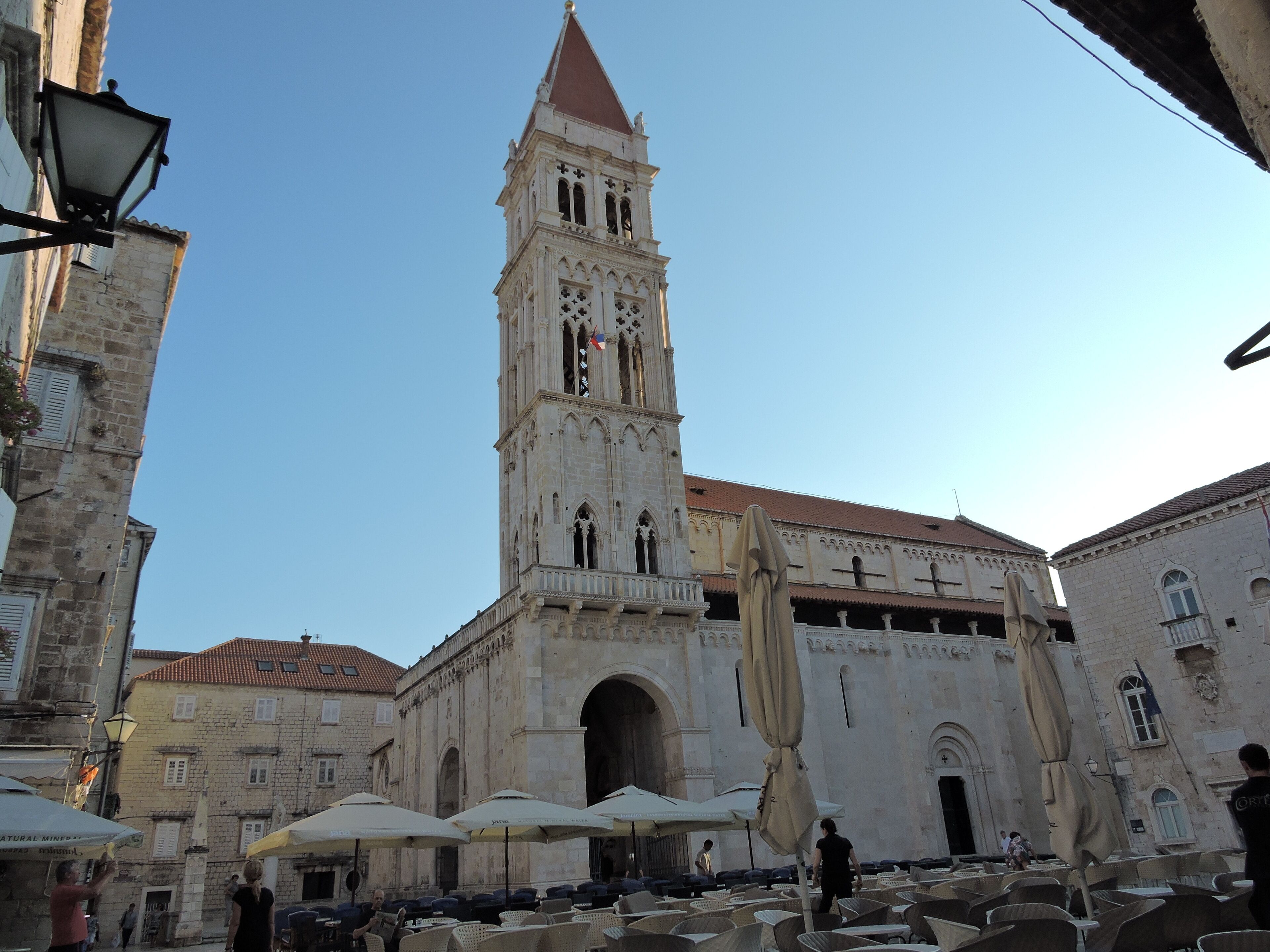 A historic building with a tall tower, outdoor seating area with umbrellas, and stone architecture.