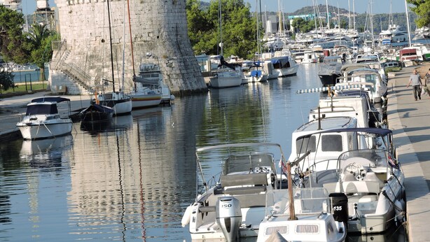 A marina with various boats docked, a stone tower, and a pedestrian walkway.
